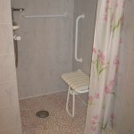 Douche de plain-pied avec siège et barre de maintien dans la chambre handicapé